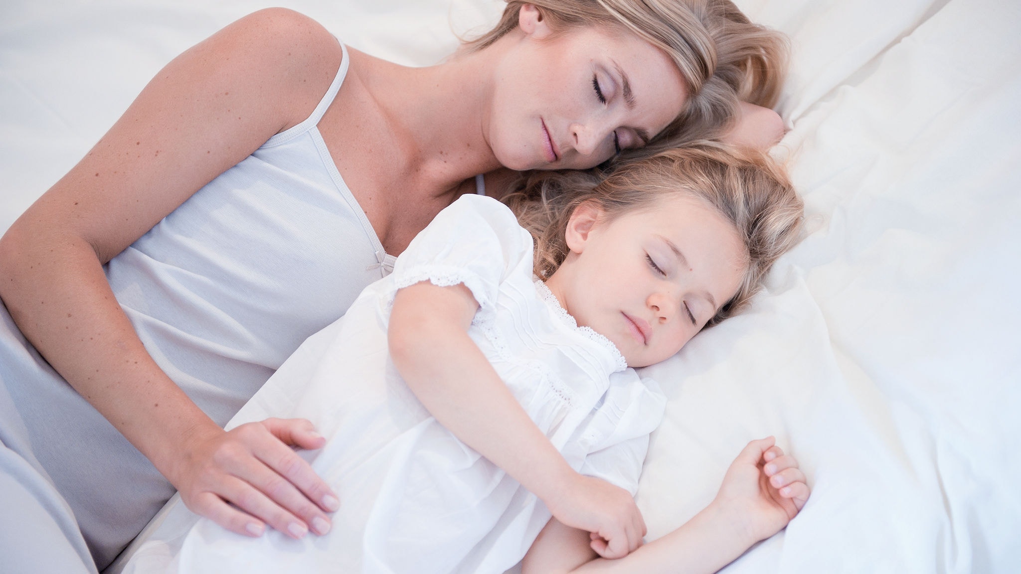 Mom and little daughter sleeping next to each other in a white bed in clean air