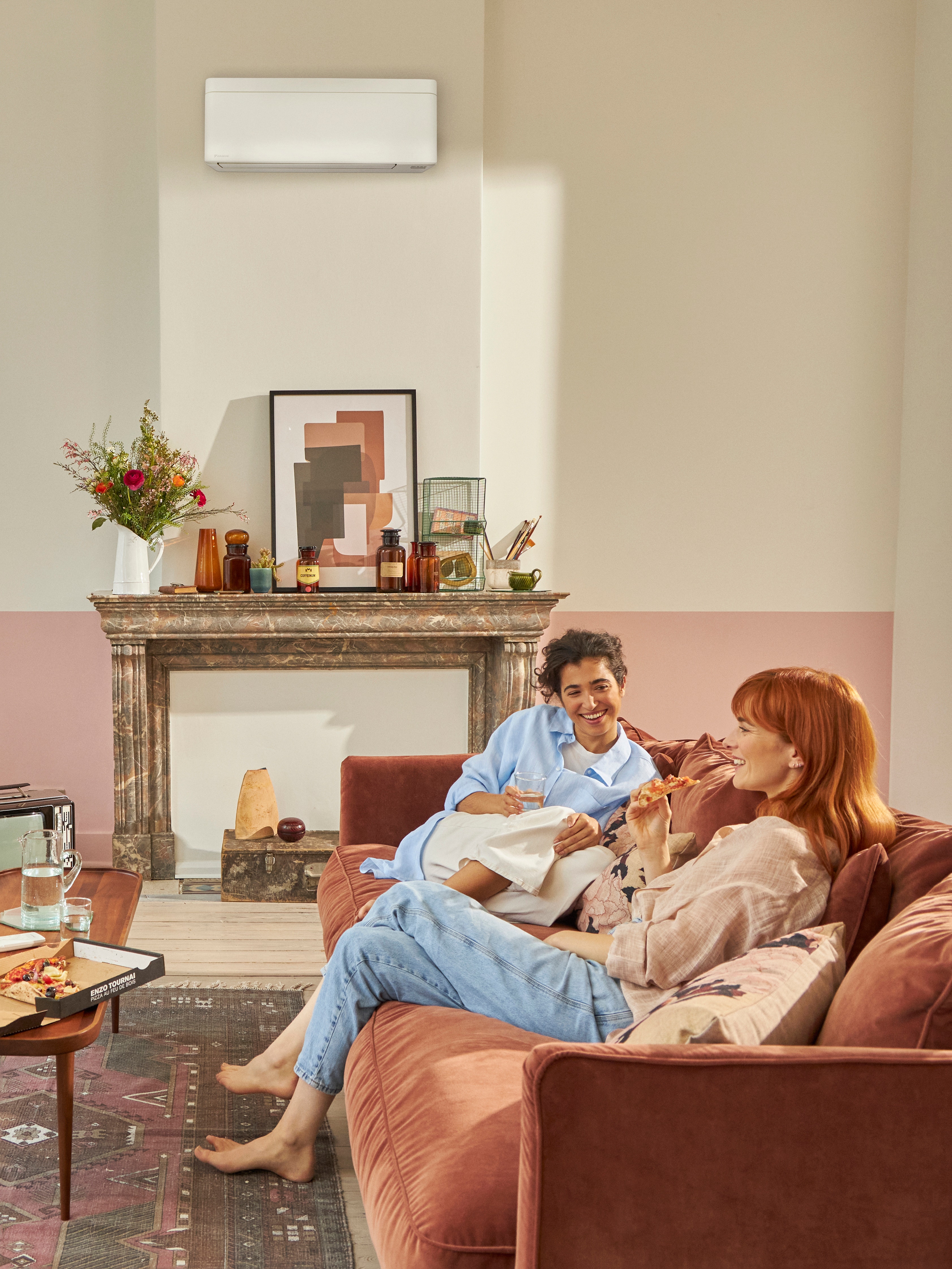 Two women sitting on the couch and talking while eating take-out pizza in a beautiful living room