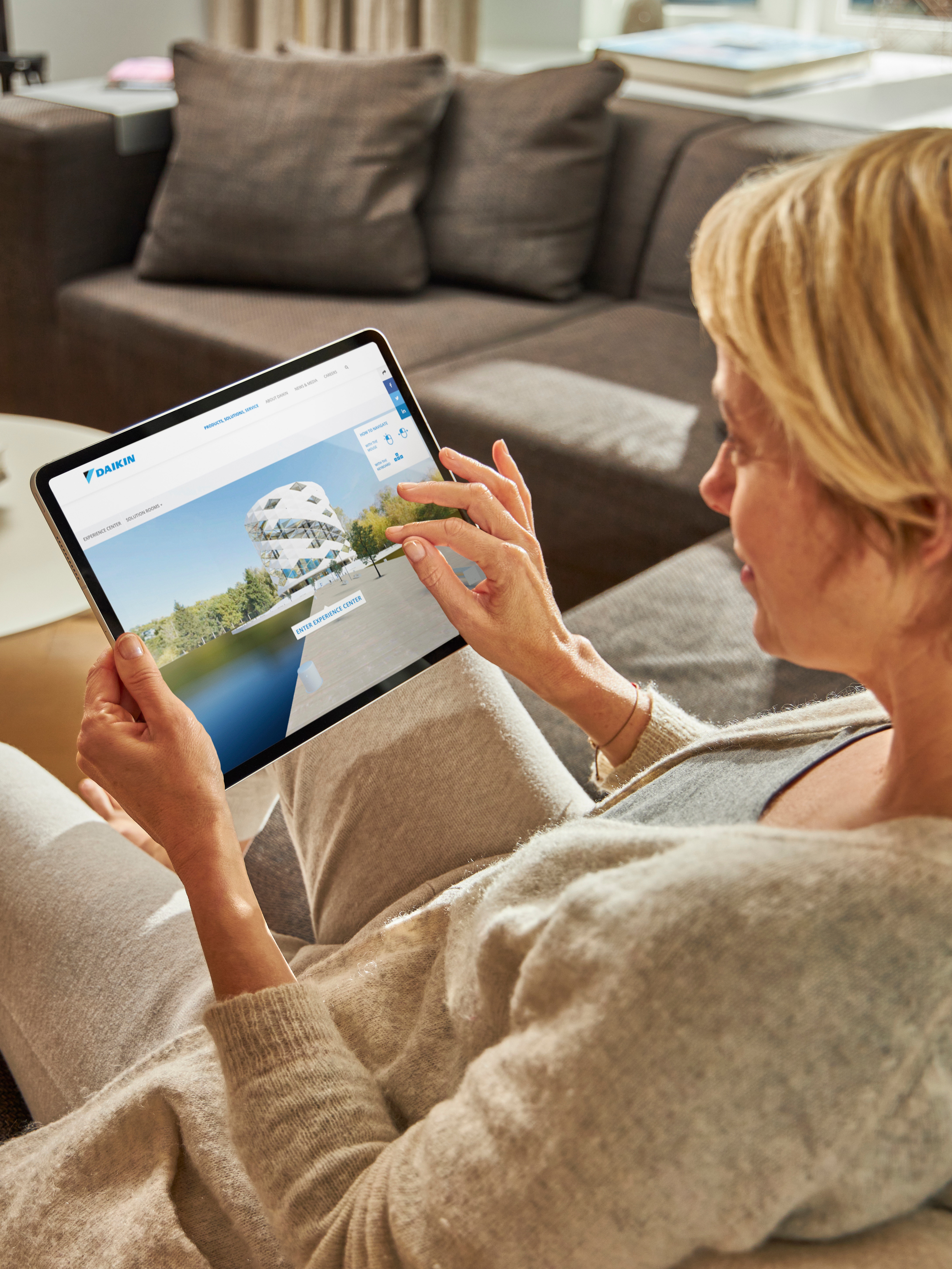 Žena sjedi na sofi i istražuje klima-uređaje u Virtualnom Experience Centru na tablet uređaju